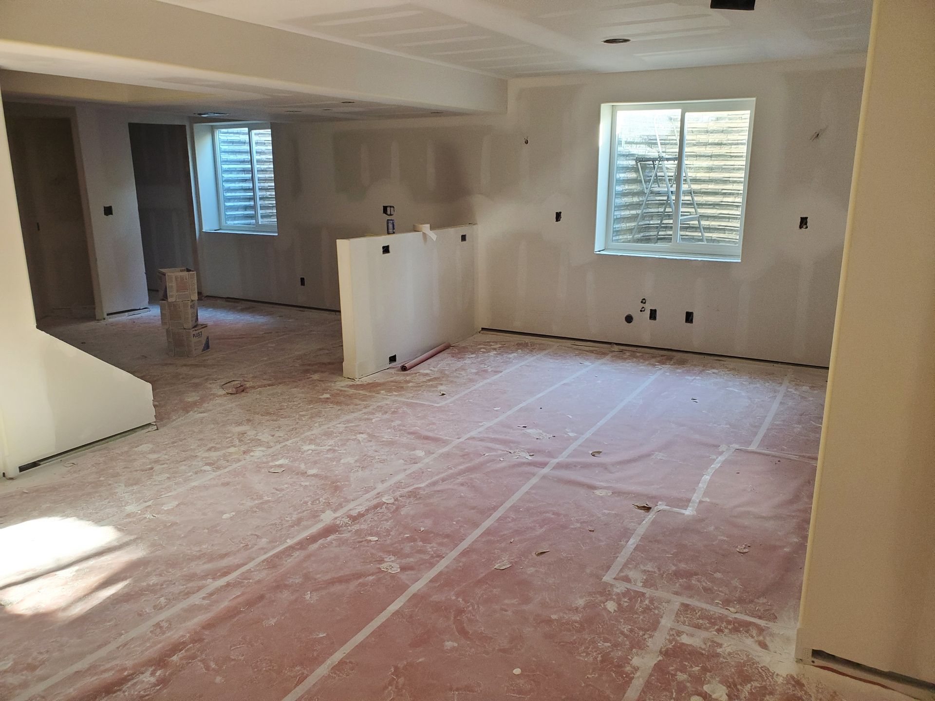 Interior of a room under construction with drywall walls, windows, and red protective covering on the floor.