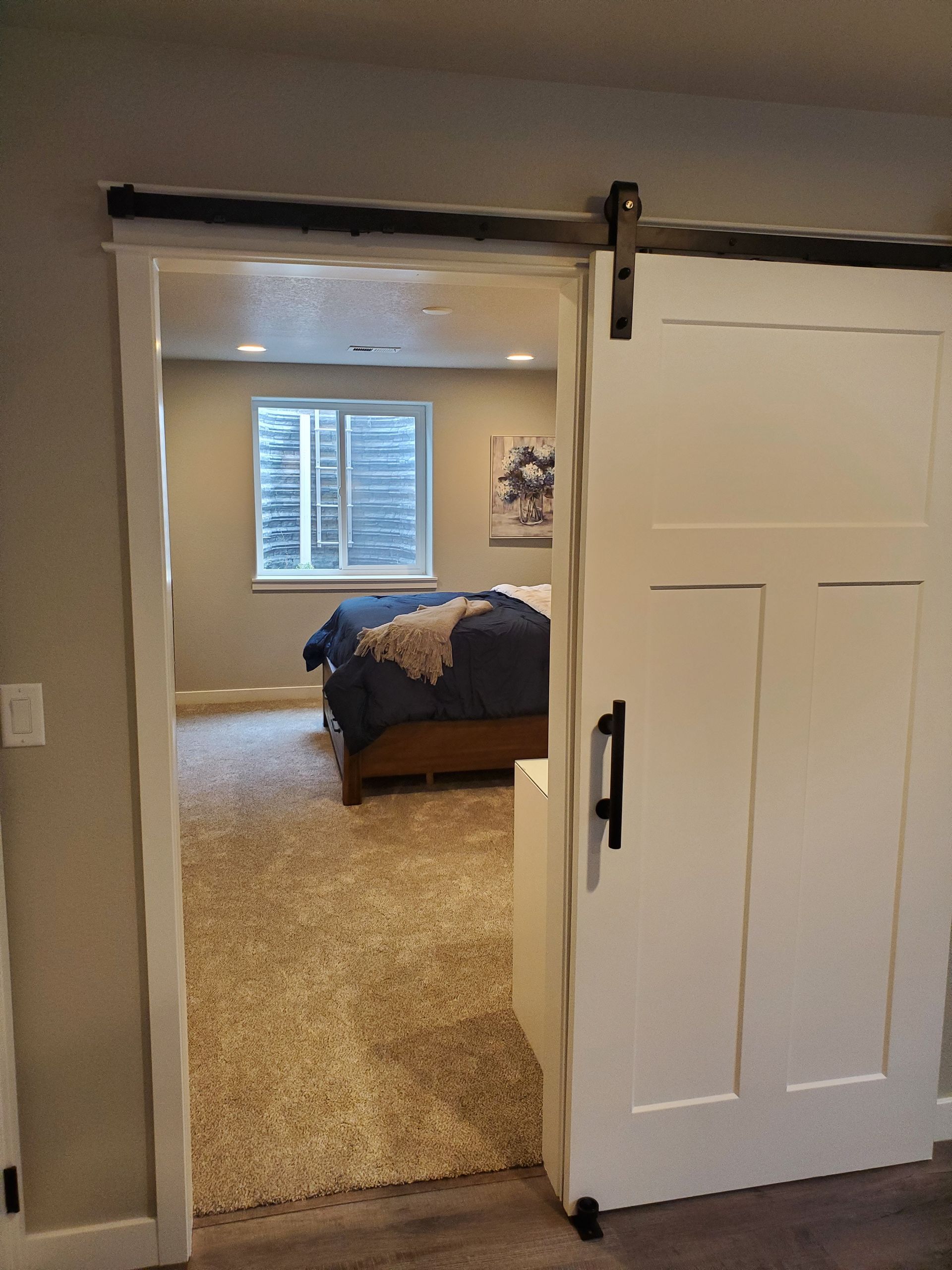Bedroom doorway with a sliding white door, open to reveal a bedroom with a bed, window and carpeted floor.