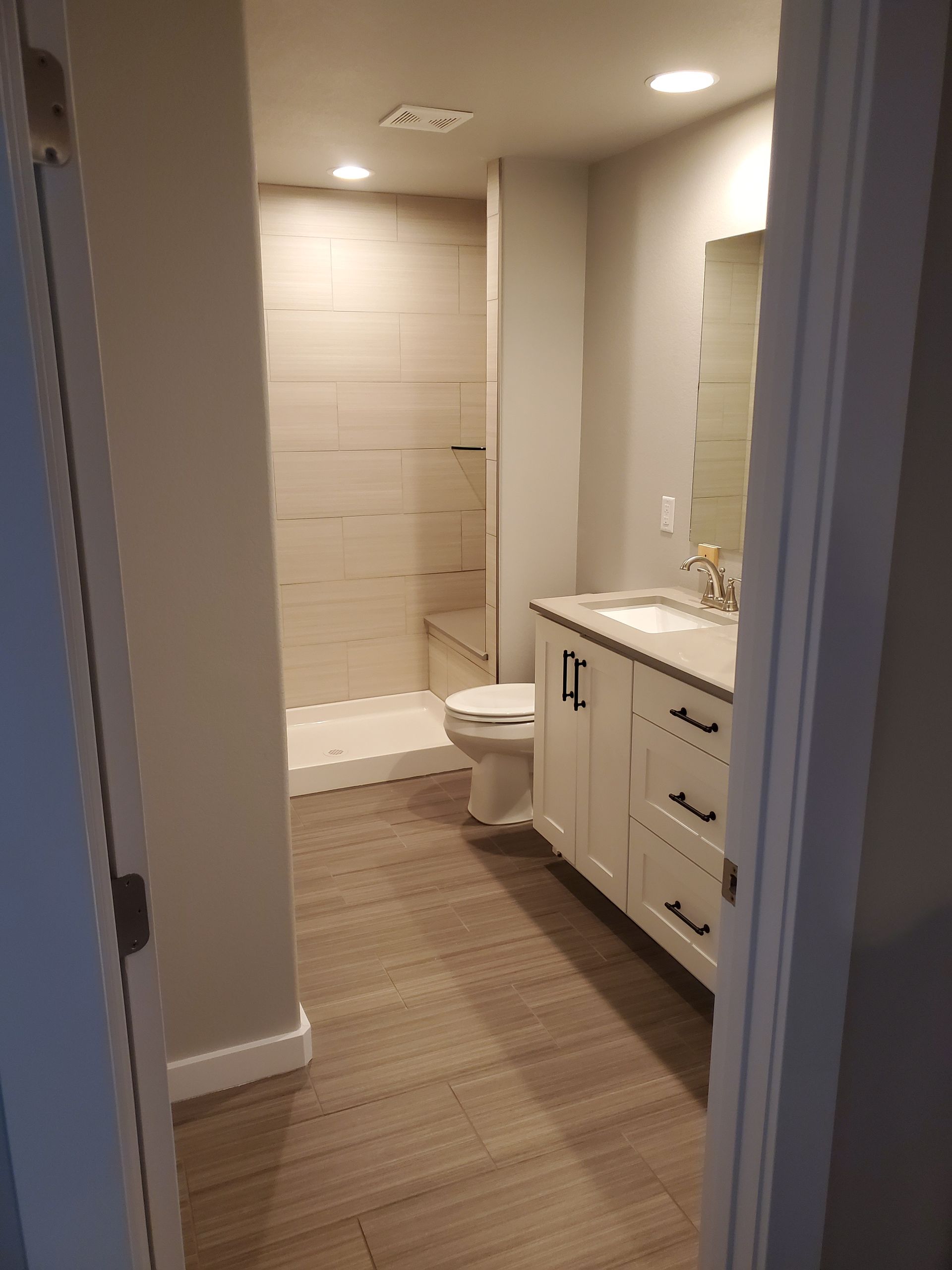 Bathroom with a white vanity, toilet, and shower; tile floor and beige walls.