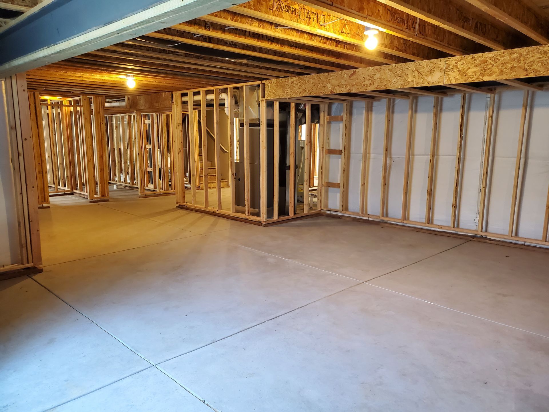 Unfinished basement with wooden studs, concrete floor, and exposed ceiling beams.