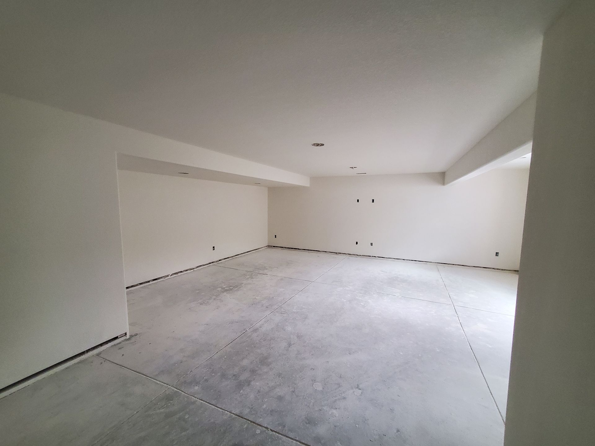 Empty, unfinished basement with white walls and concrete floor.