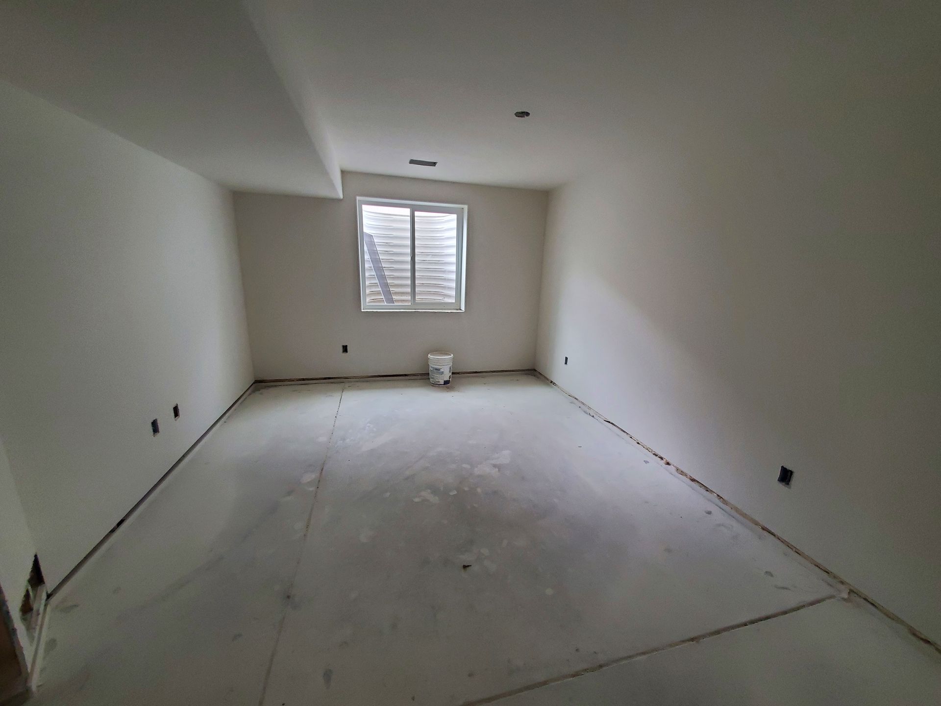 Empty room with window, white walls, concrete floor, and electrical outlets.