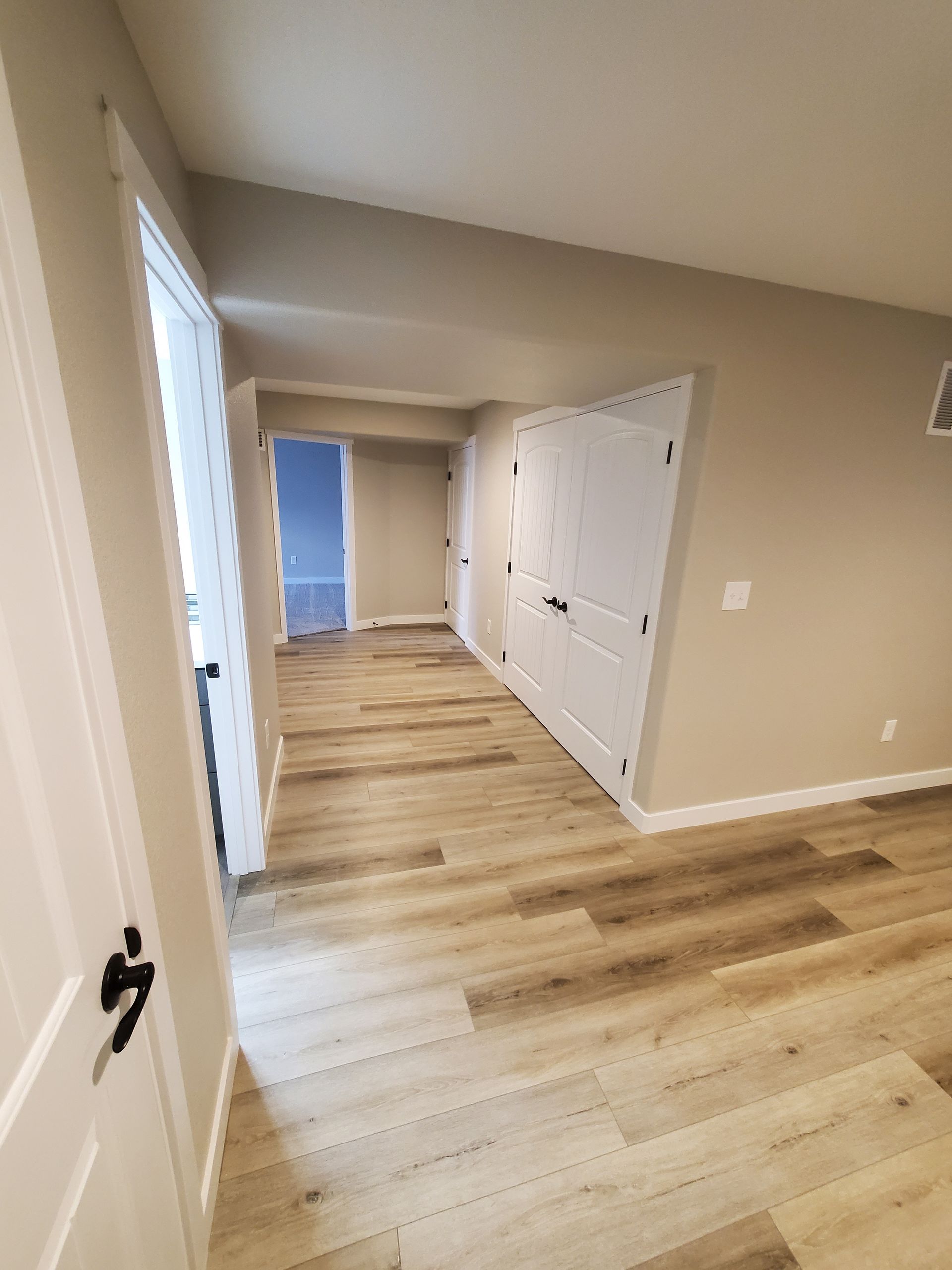 Hallway with light wood-look flooring, beige walls, and white doors.
