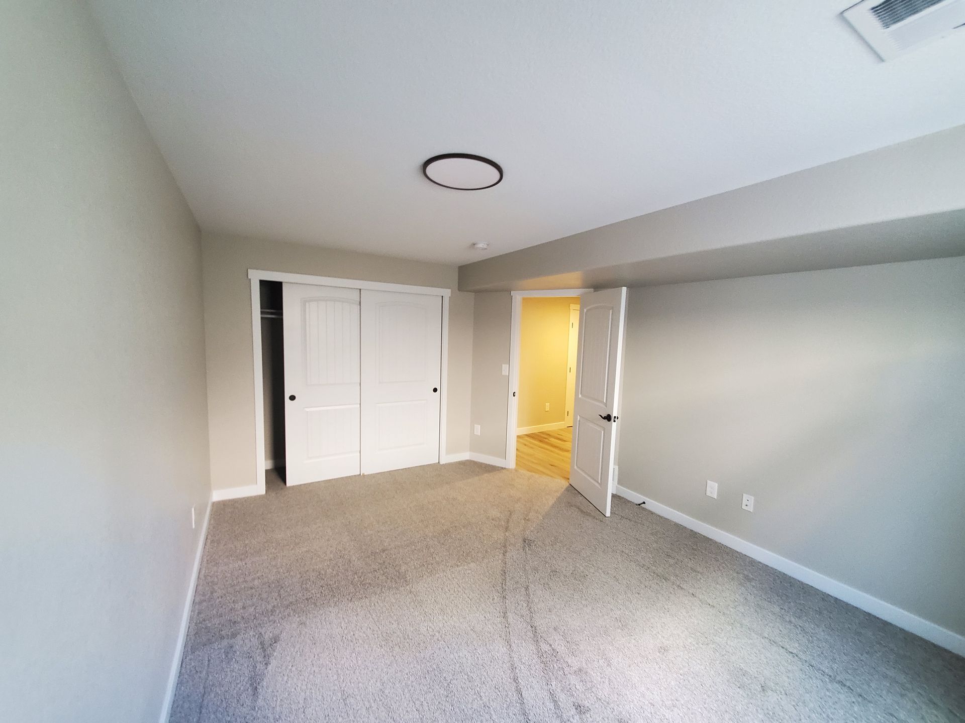 Empty bedroom with gray carpet, white closet doors, and an open door to a hallway.