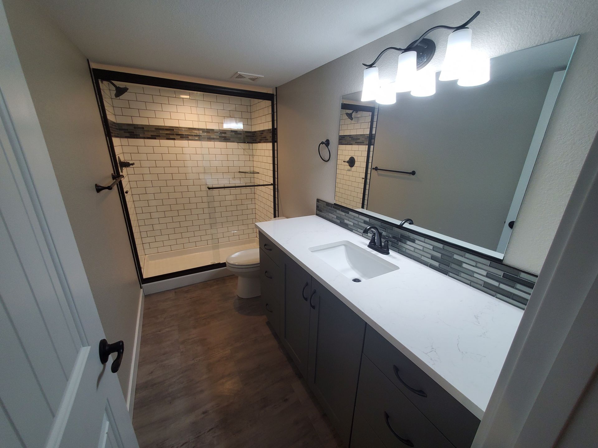 Bathroom with a gray vanity, white countertop, and glass shower.