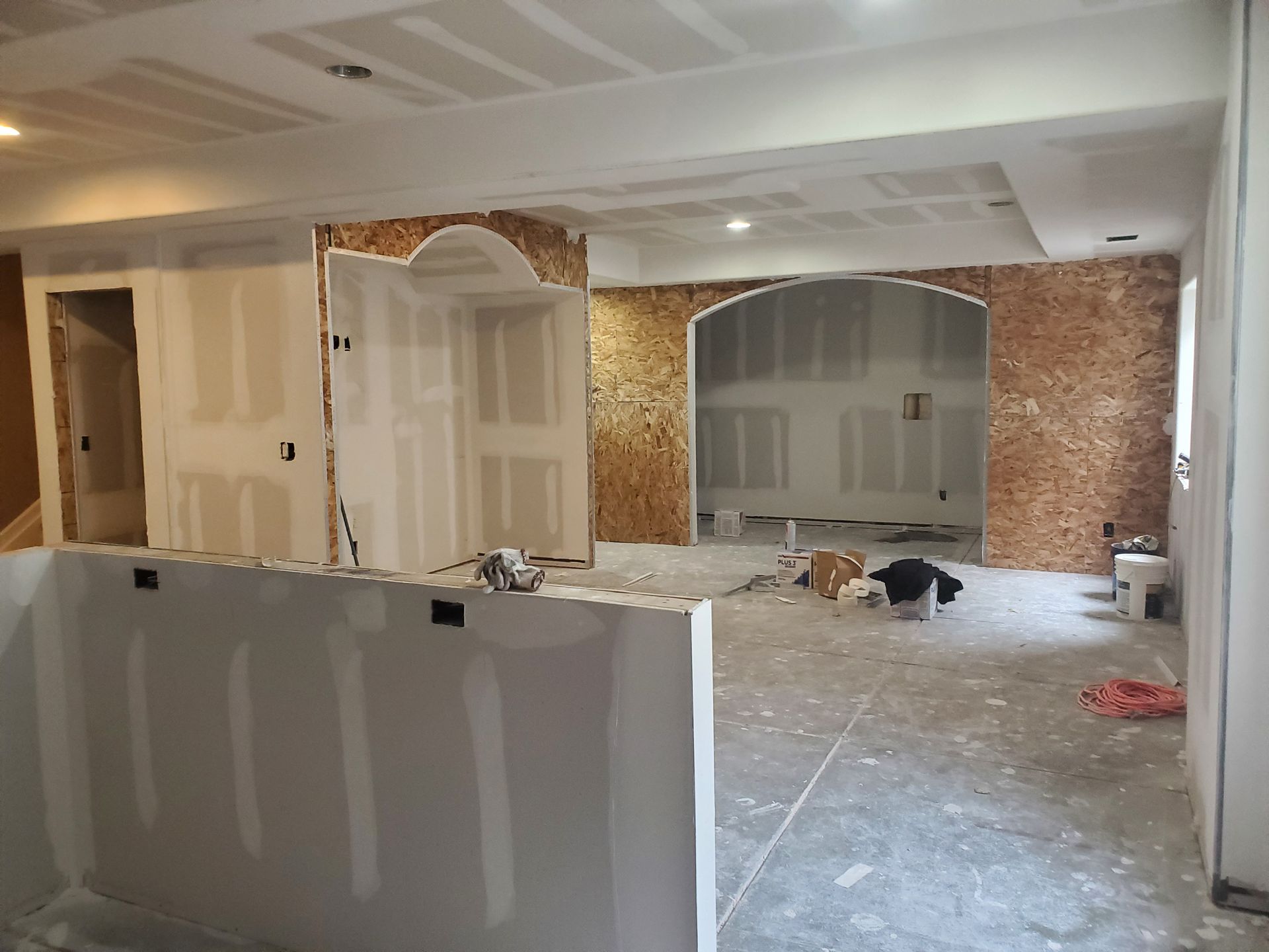 Interior construction site with drywall, exposed particle board, and recessed lighting.