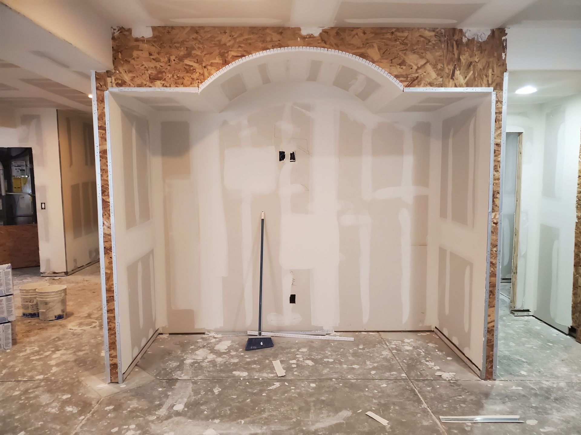 Interior framing with drywall partially installed, showing an arched niche, construction site.