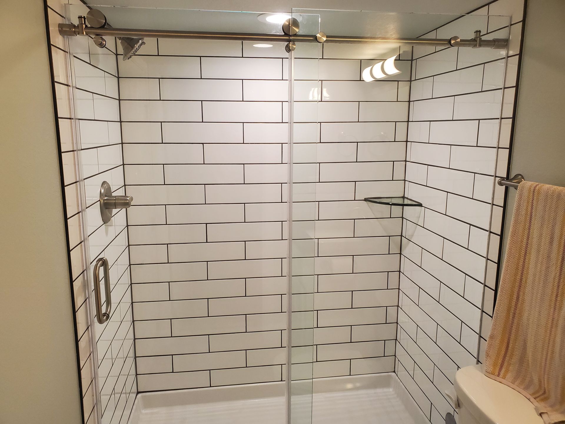 Shower with white subway tile walls, glass doors, and a towel on the right.