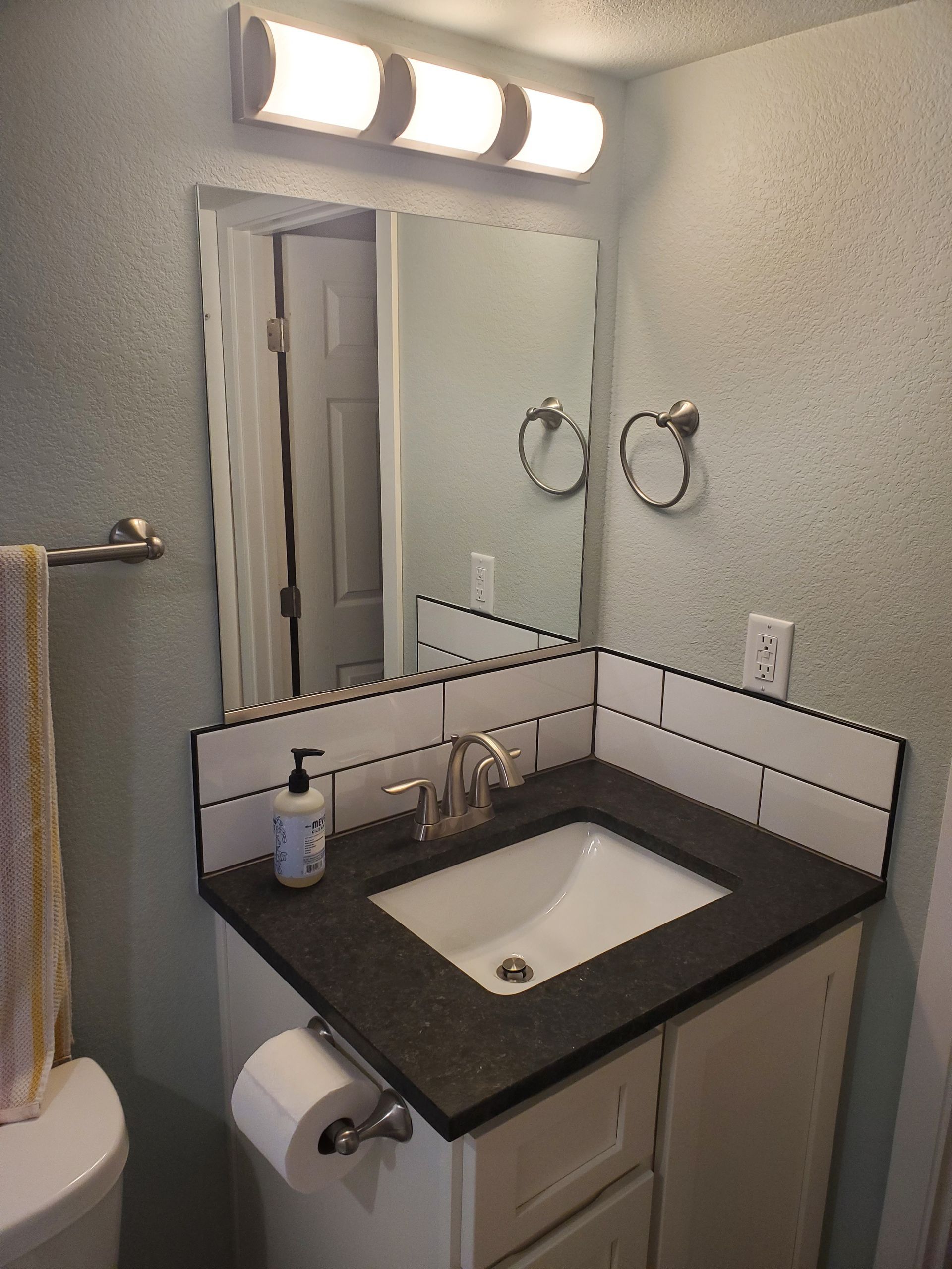 Bathroom vanity with white sink, black countertop, white subway tile backsplash, and mirror.