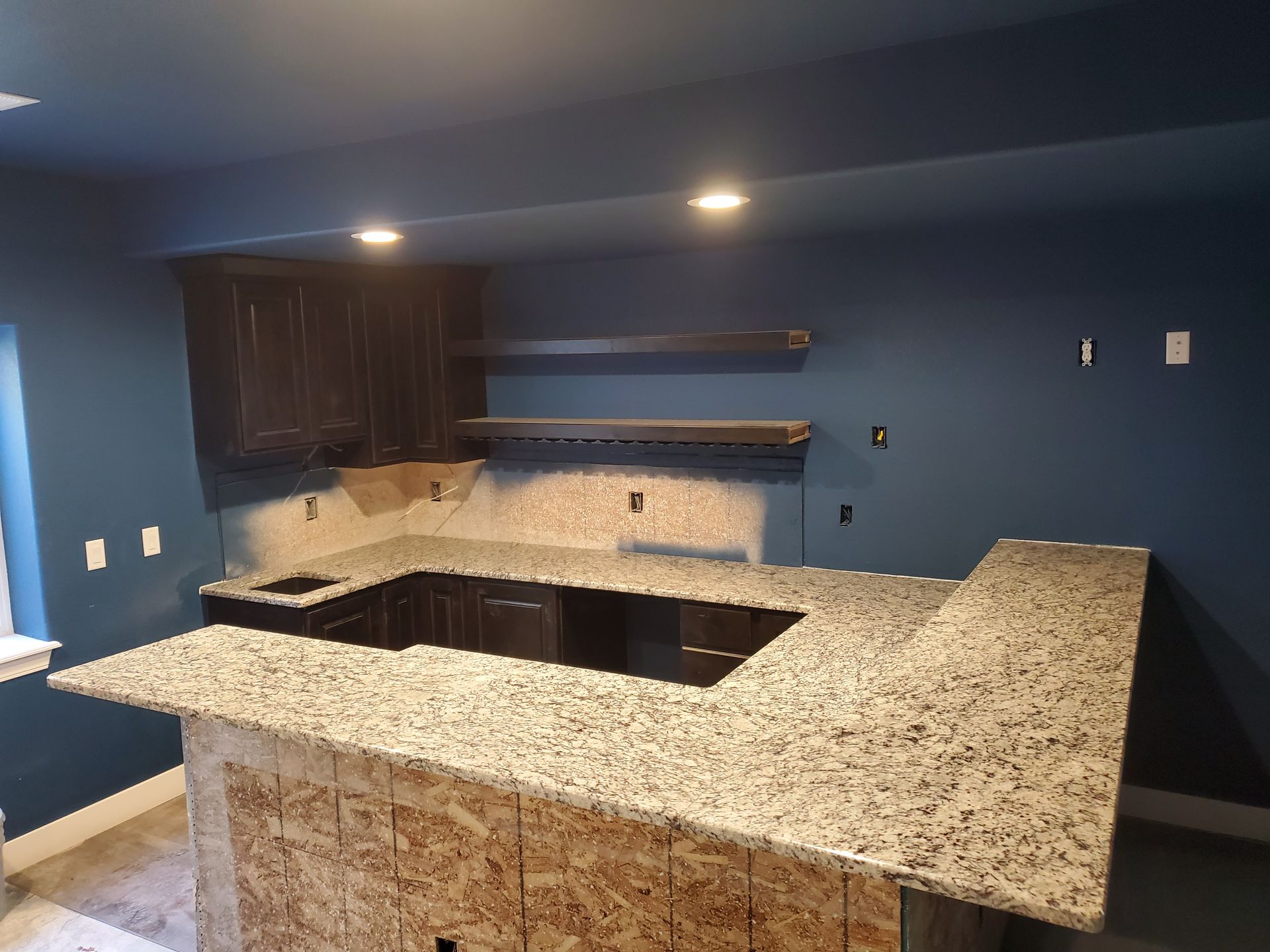 Basement bar under construction with granite countertops, dark cabinets, and blue walls.