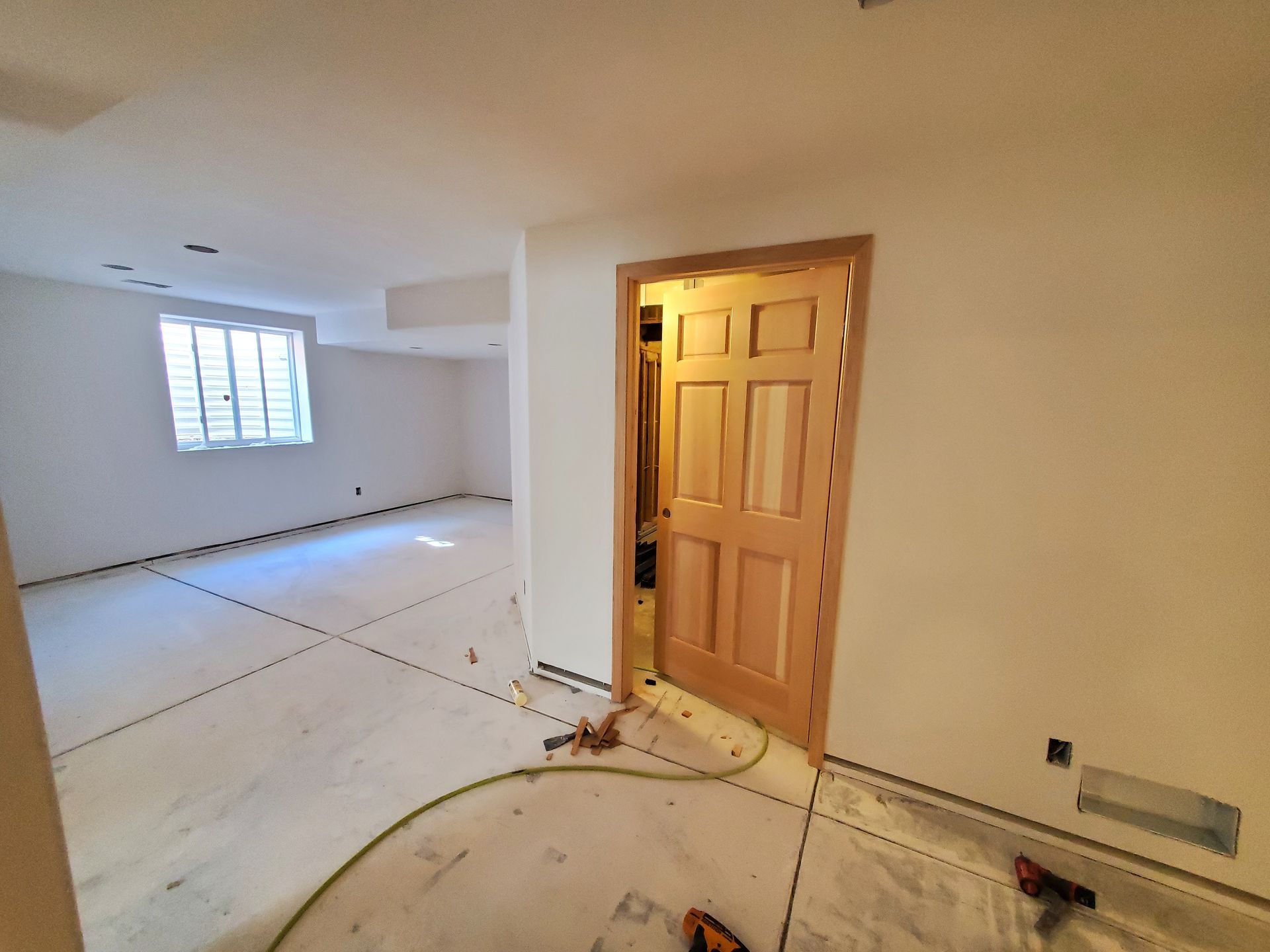 Interior view of a room under construction; doorway, window, exposed concrete floor, and tools present.