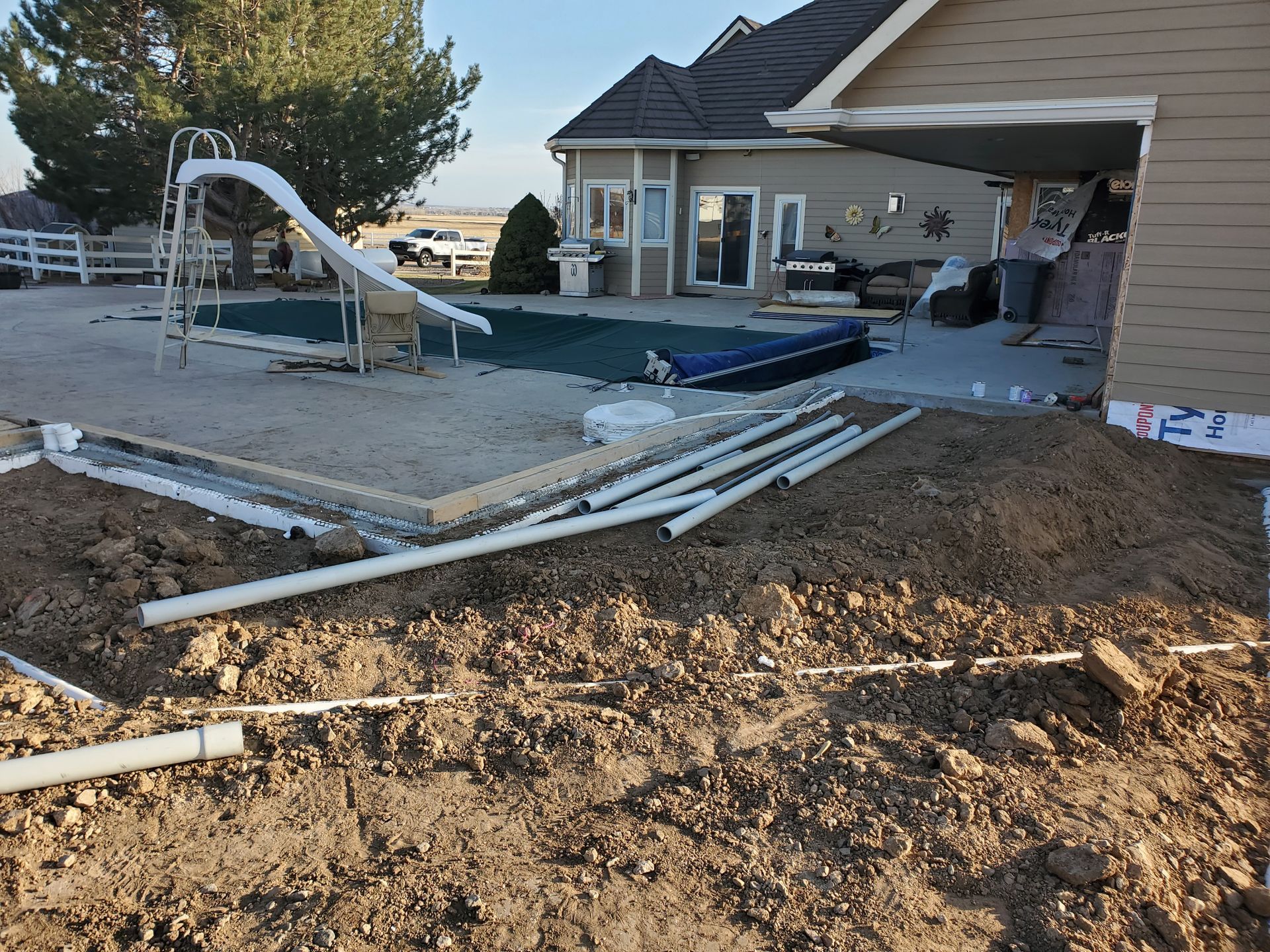 Backyard under construction with pool, pipes, and dirt.