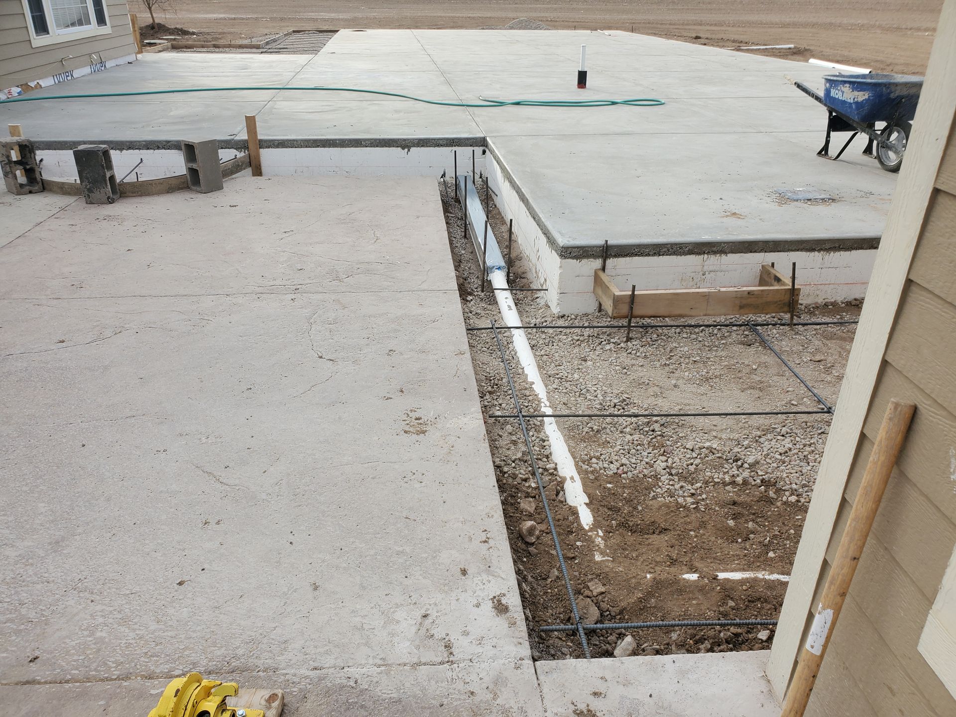 Concrete patio under construction with exposed rebar and drainage pipes.