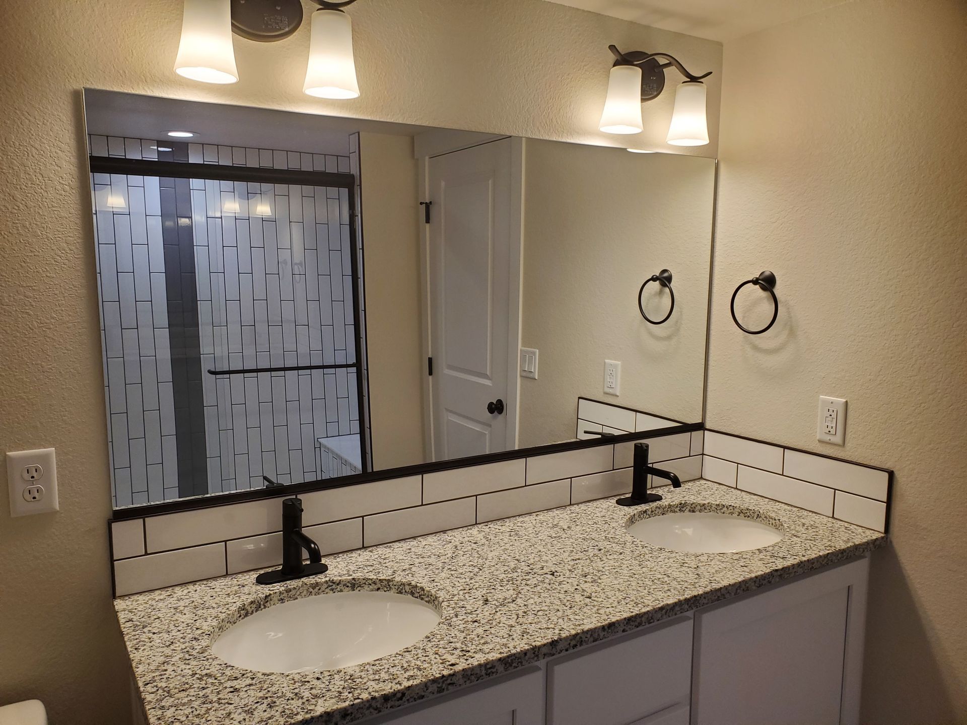 Bathroom with double sink granite countertop, large mirror, and black fixtures and lighting.