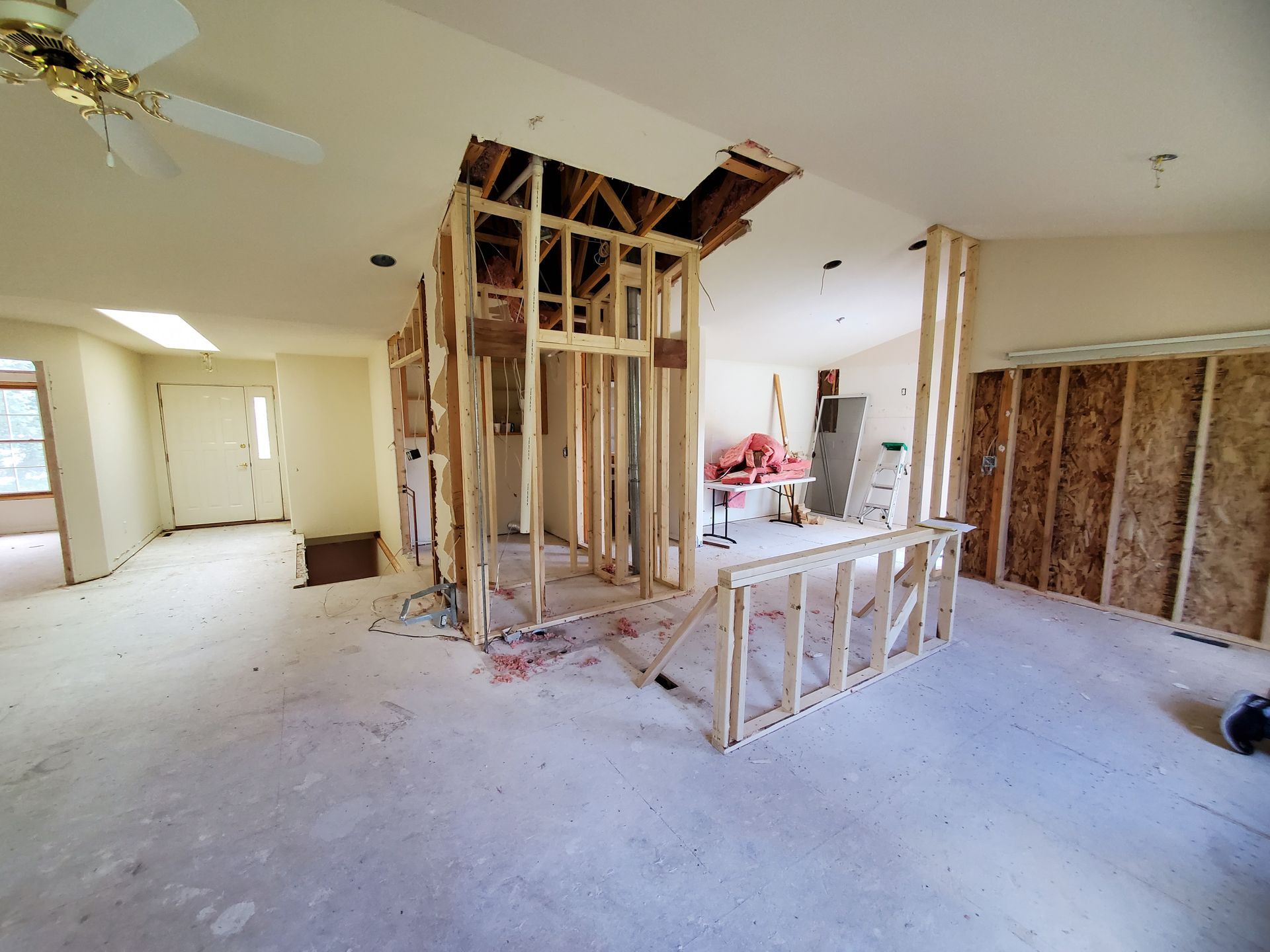 Interior room under renovation with exposed wood framing. Drywall removed, ceiling cut open.
