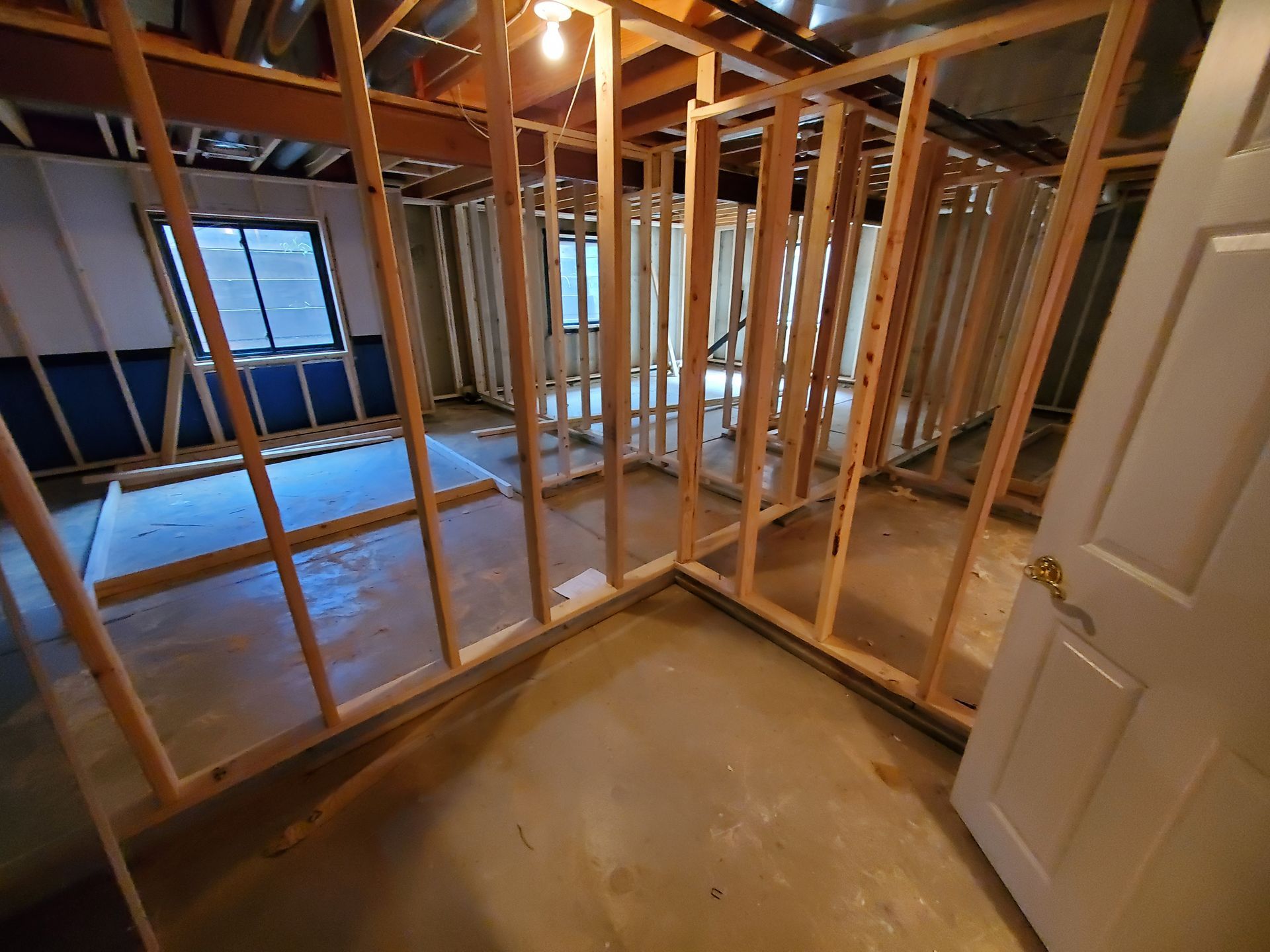 Basement renovation: wooden wall framing, a window, a door, and exposed concrete floor.