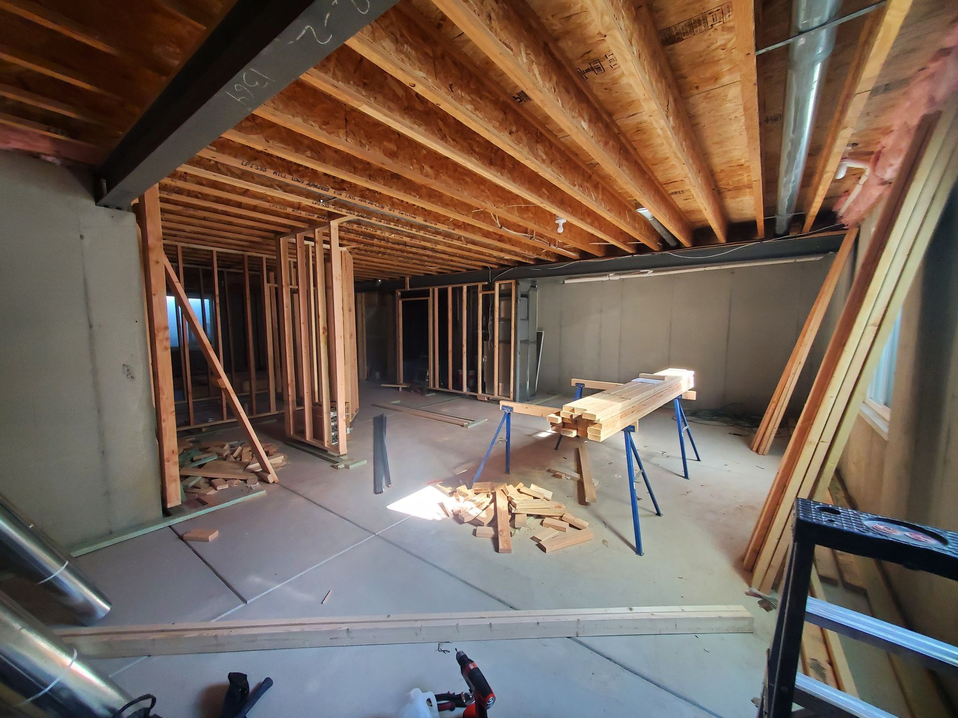 Basement under construction; wood framing, concrete floor, sawhorses, and exposed ceiling beams.