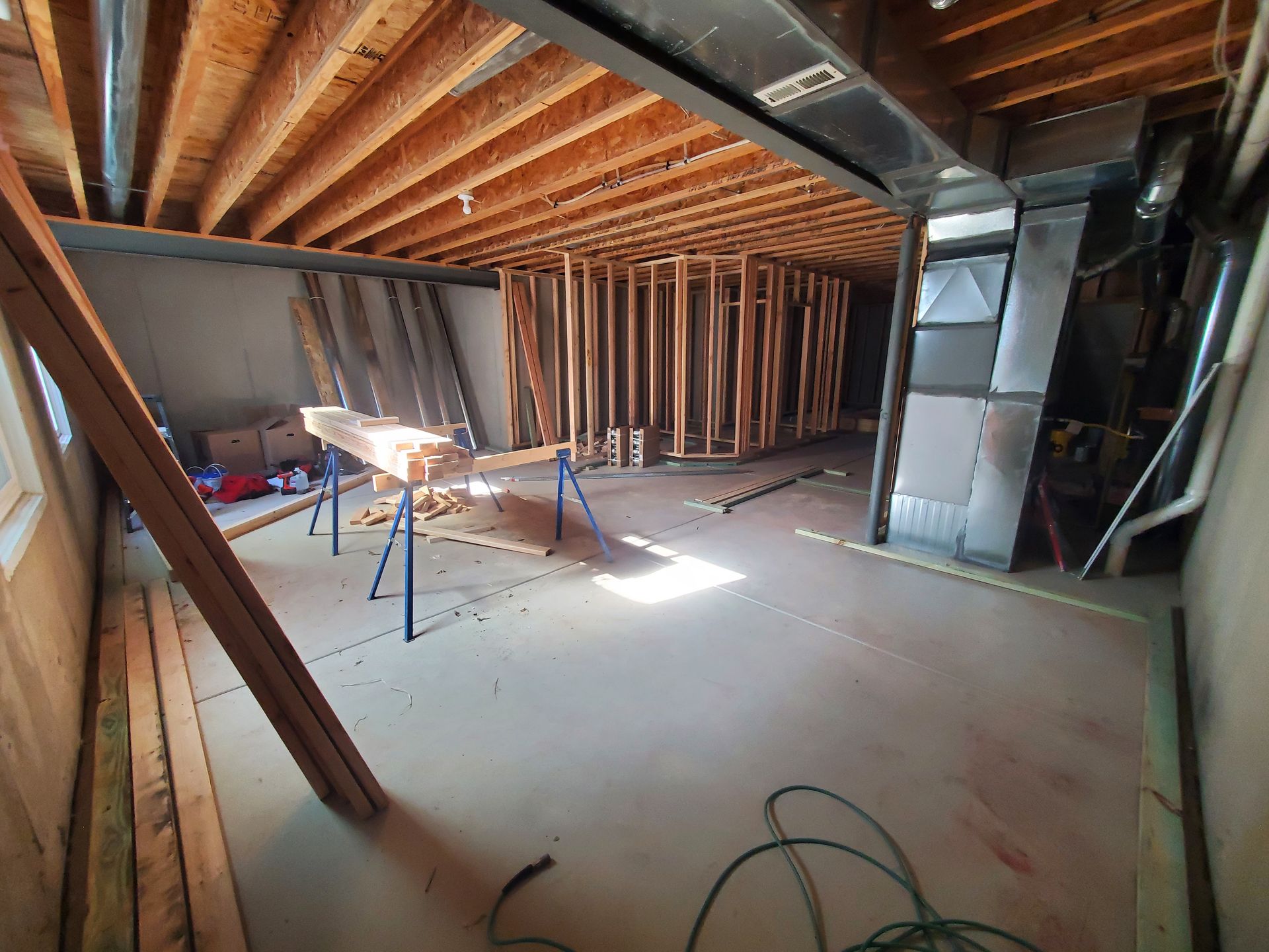Basement under construction with exposed wooden beams, framing, and a concrete floor.