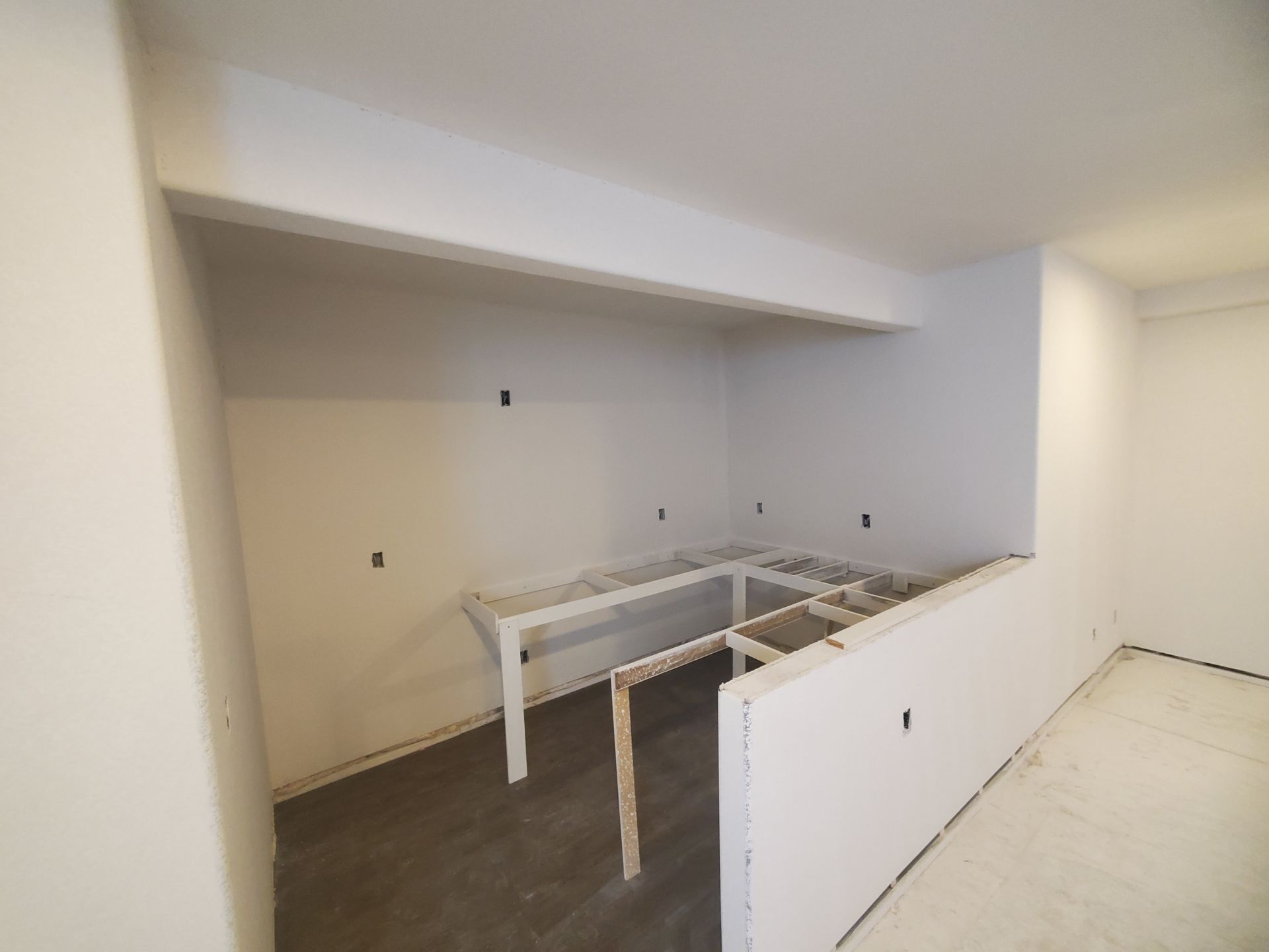 Empty kitchen area under construction: white walls, unfinished countertops, gray flooring.