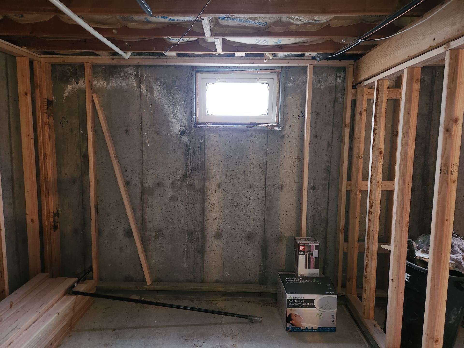 Basement wall with window, framed with wooden studs. Concrete wall is damp and stained.