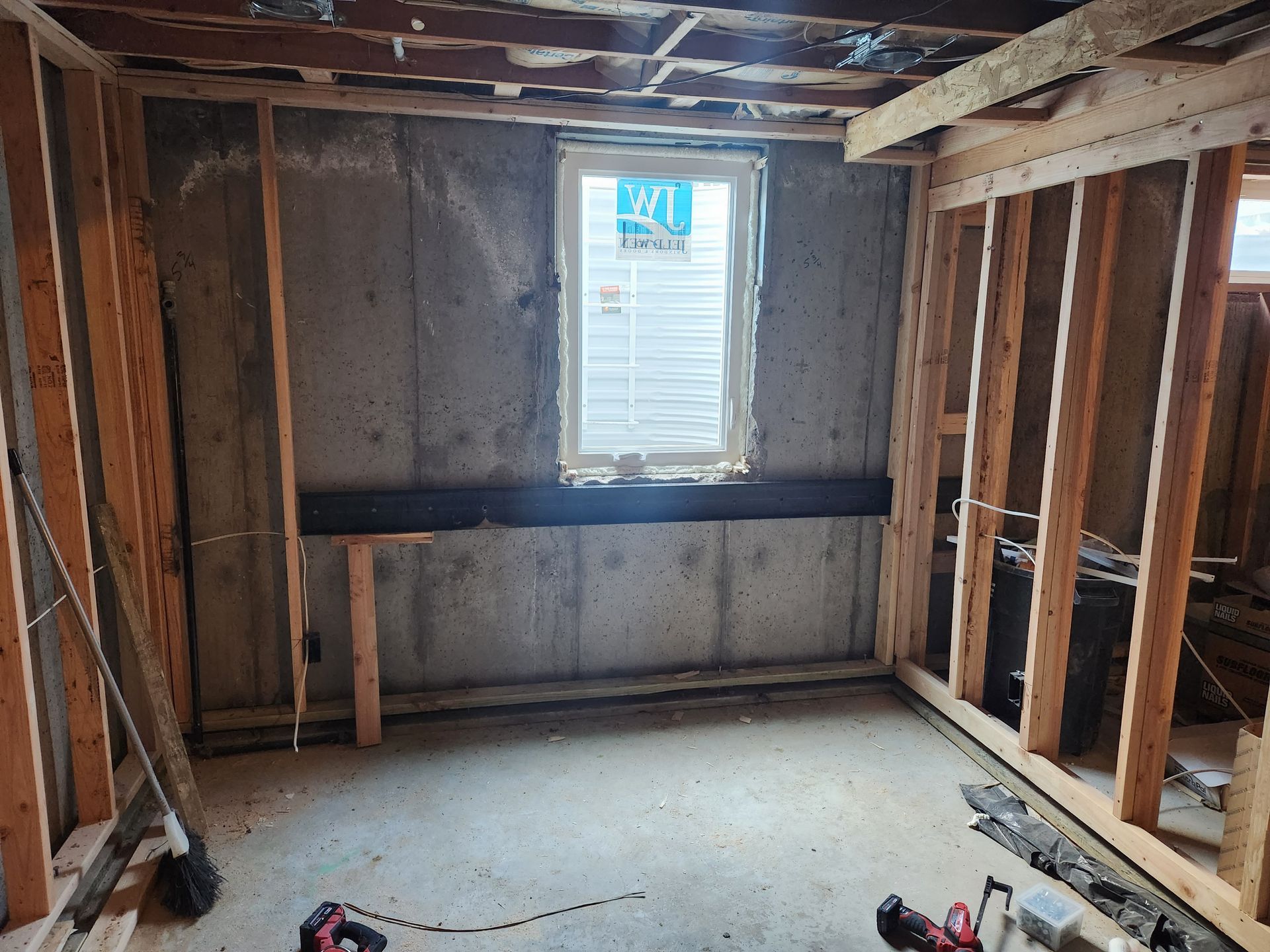 Basement room under construction, with exposed wooden framing, concrete walls, and a window.