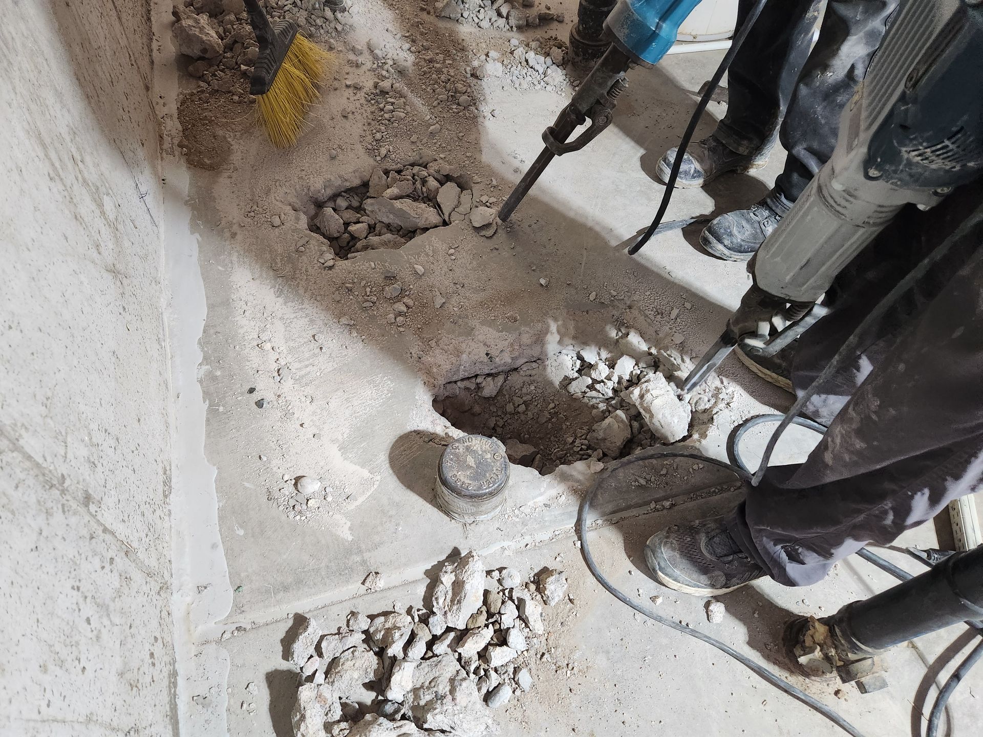 Workers using jackhammers to break concrete on a floor, creating a trench.