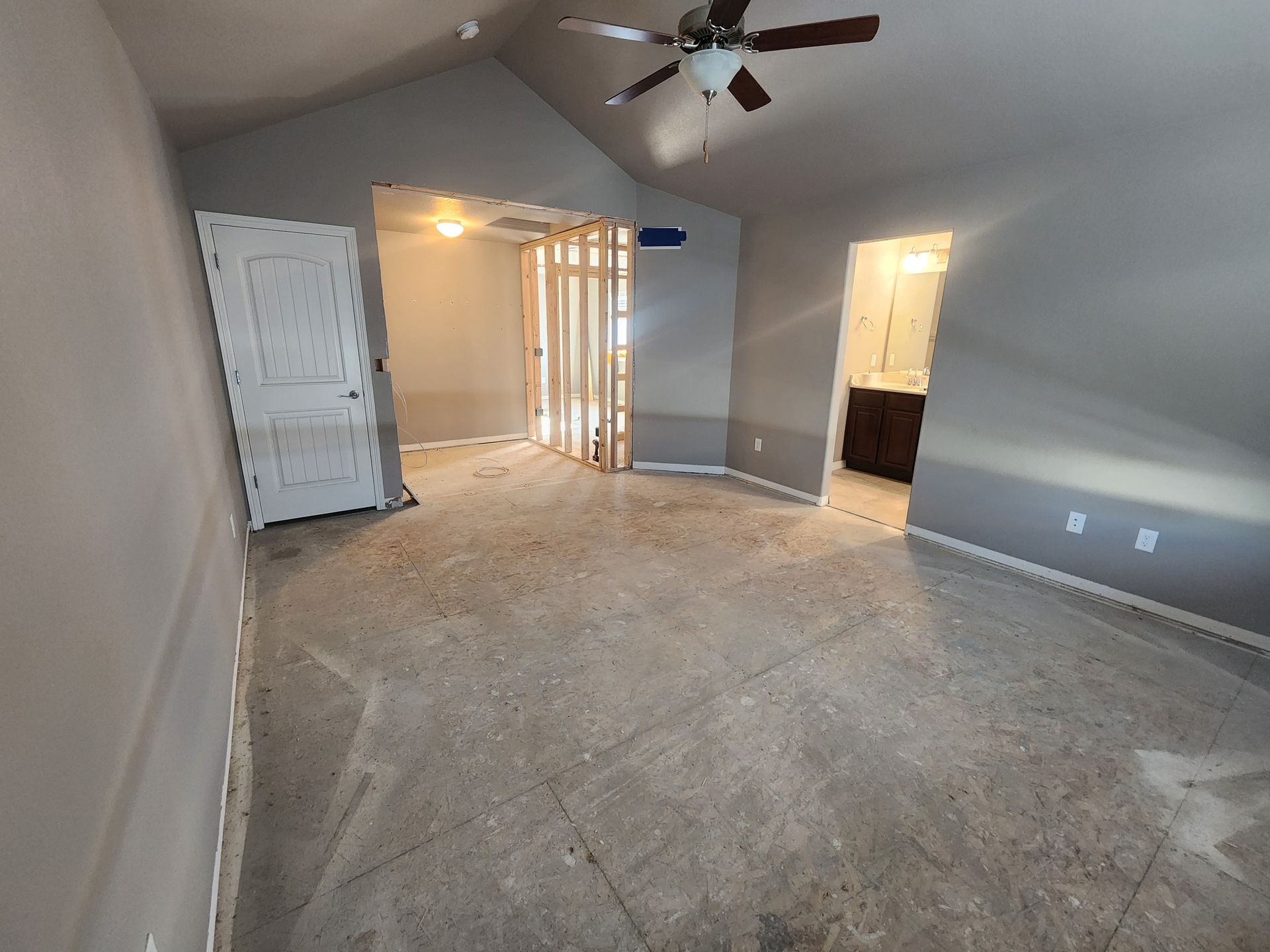 A room with gray walls, concrete floor, door, and open doorway, possibly under construction.