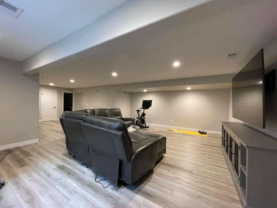 Spacious finished basement with gray walls, a reclining sofa, workout equipment, a TV, and wood-look flooring.