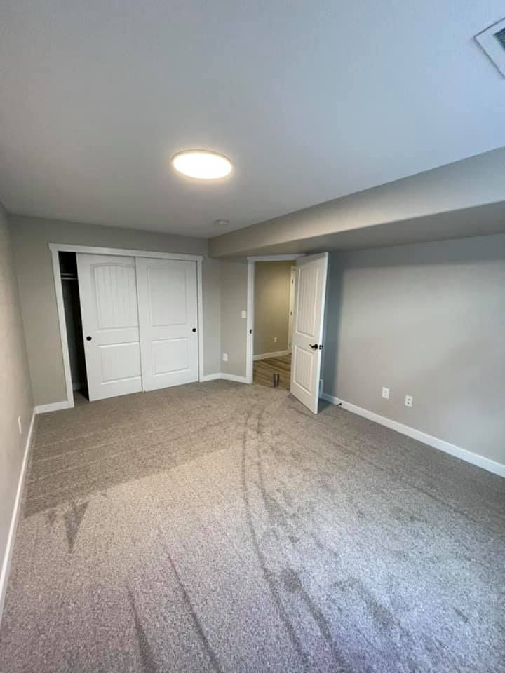Empty bedroom with gray carpet, white doors, and a recessed ceiling light.
