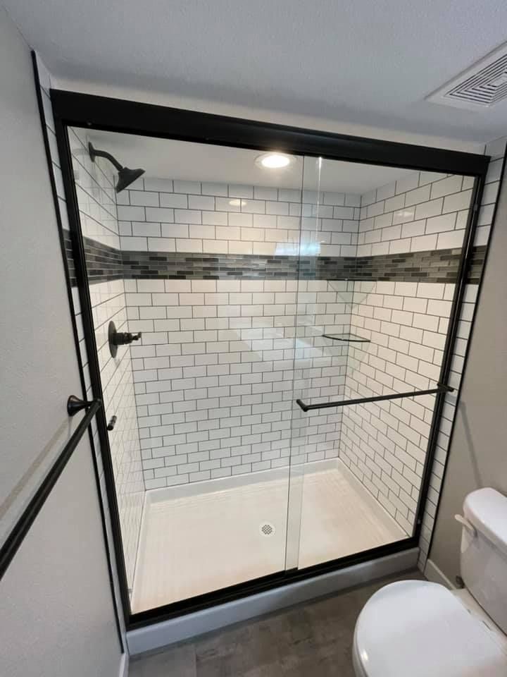 Modern shower with black-framed glass doors, white subway tile, a dark decorative band, and a toilet to the right.