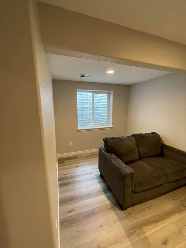 A small beige room with a couch, window, and light-colored wood-look flooring.