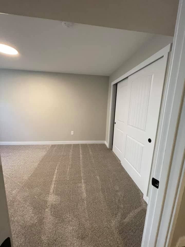 Empty bedroom with light gray walls and carpet, a sliding door, and white trim.