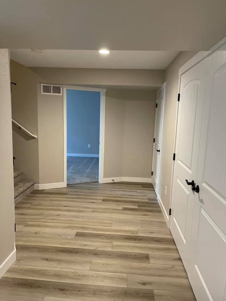 Hallway with wood-look flooring, leading to a room. Two white doors on the right side, beige walls, recessed lighting.