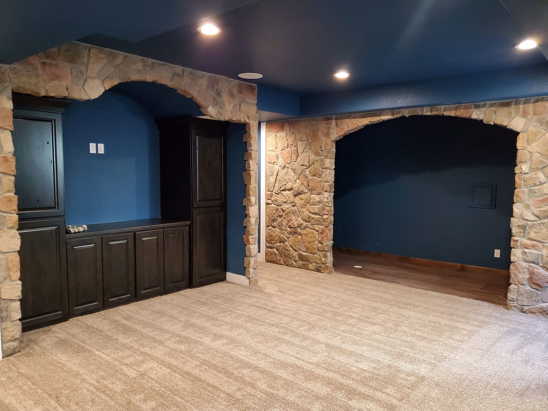 Room with stone arches, blue walls, dark cabinets, and beige carpet.