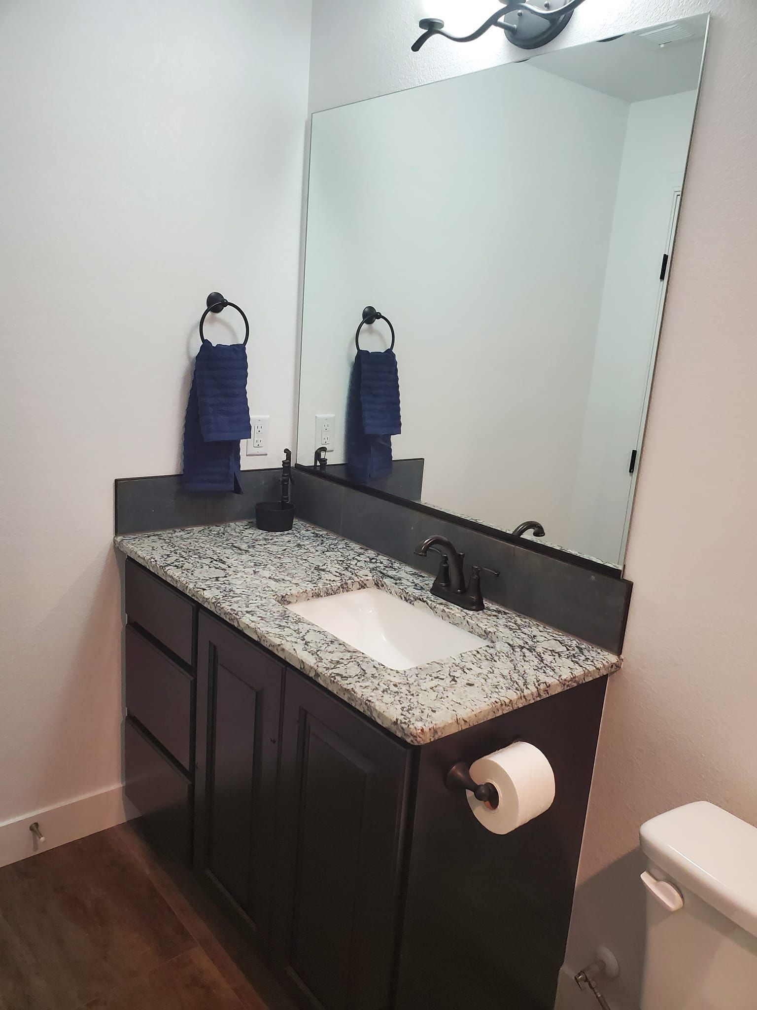 Dark vanity with granite countertop, large mirror, and two blue towels in a bathroom.