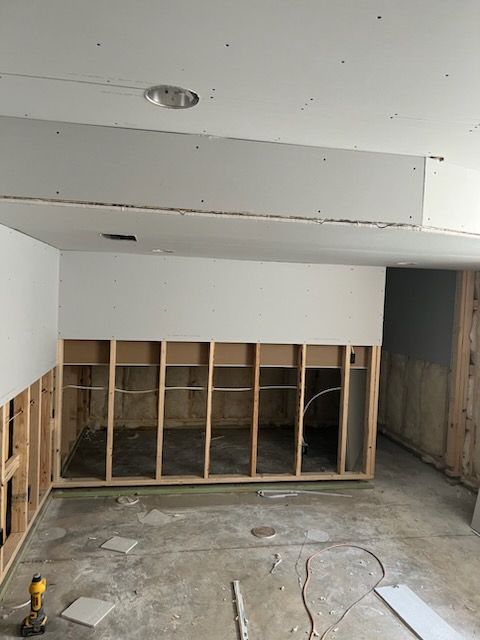 Construction site interior with exposed wall studs, drywall, and unfinished concrete floor.