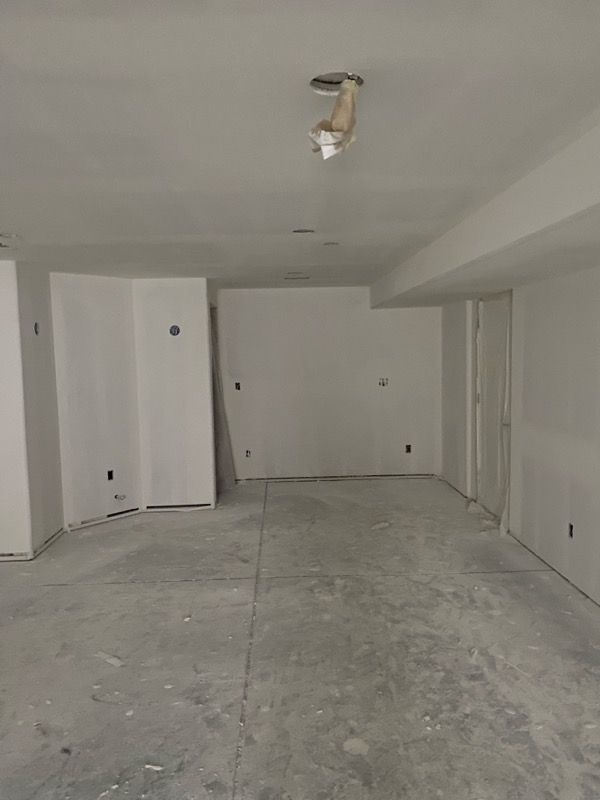 Empty, unfinished basement with concrete floor and white walls. Electrical outlets and exposed light fixture visible.