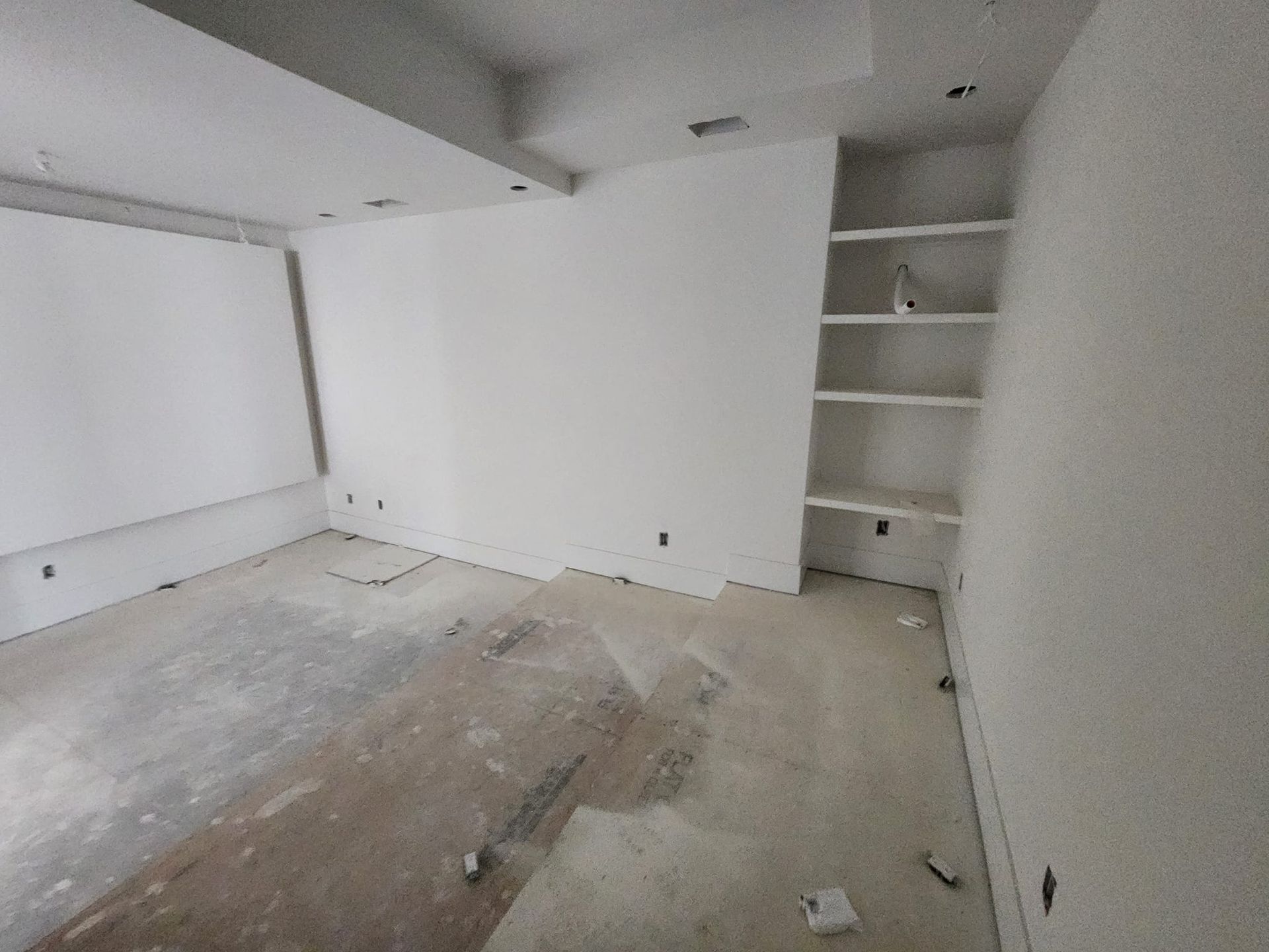 Empty room under construction, white walls, built-in shelves, concrete floor.
