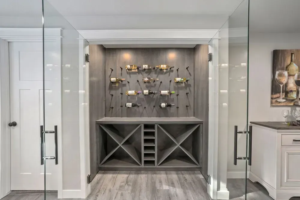 Wine cellar with grey wood shelving and modern wine racks framed by glass doors.