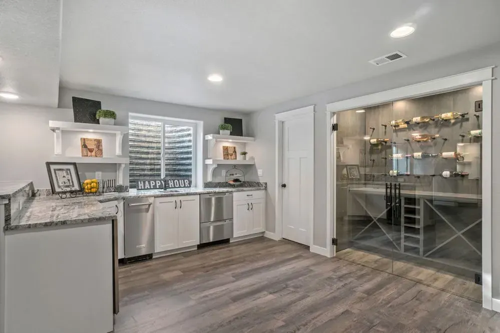 A basement kitchen with a wine cellar. White cabinets, gray countertops, and a glass door.