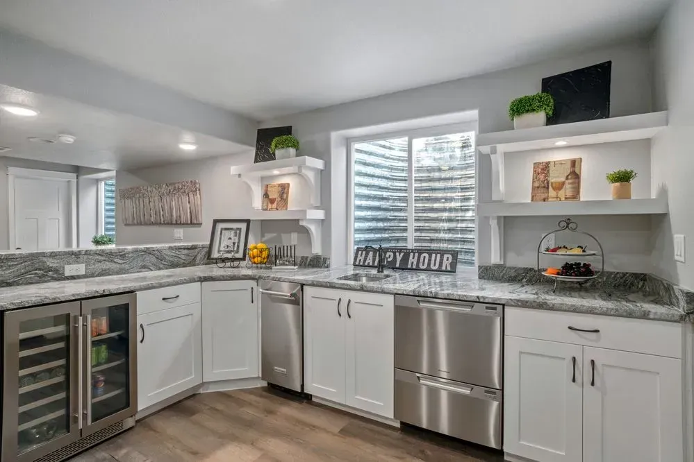 White kitchen with stainless steel appliances, gray countertops, and a window well.