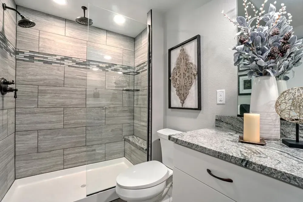 Modern bathroom with gray tiled shower, toilet, vanity, and decorative accents.