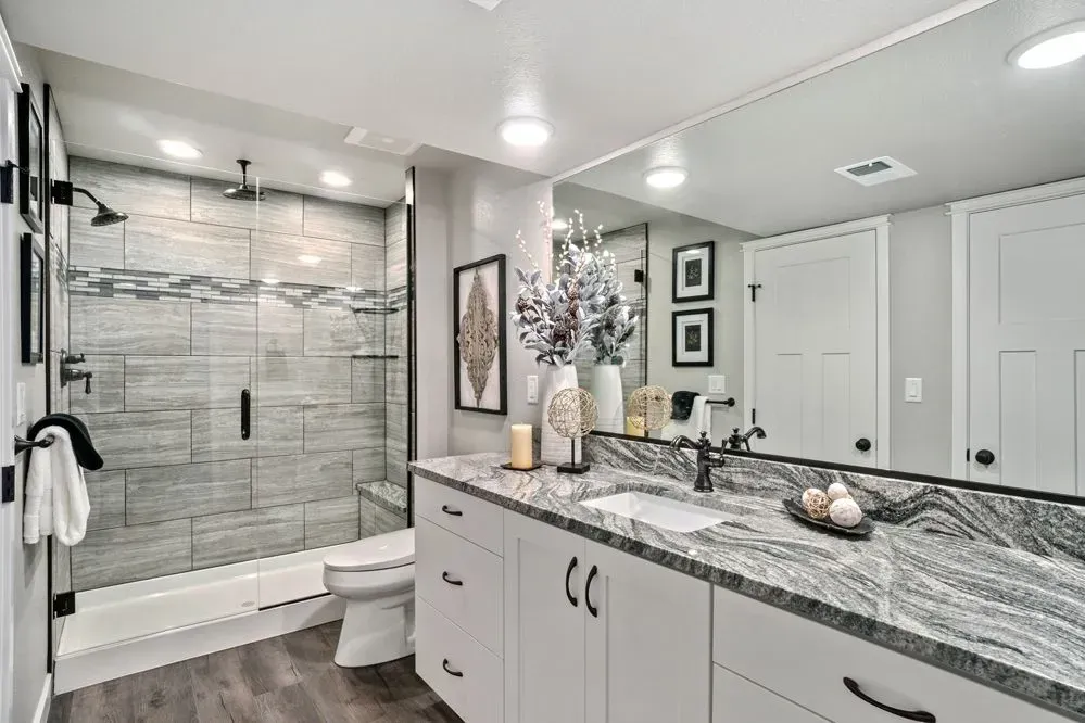 Bathroom with a gray tiled shower, white vanity, and a large mirror.