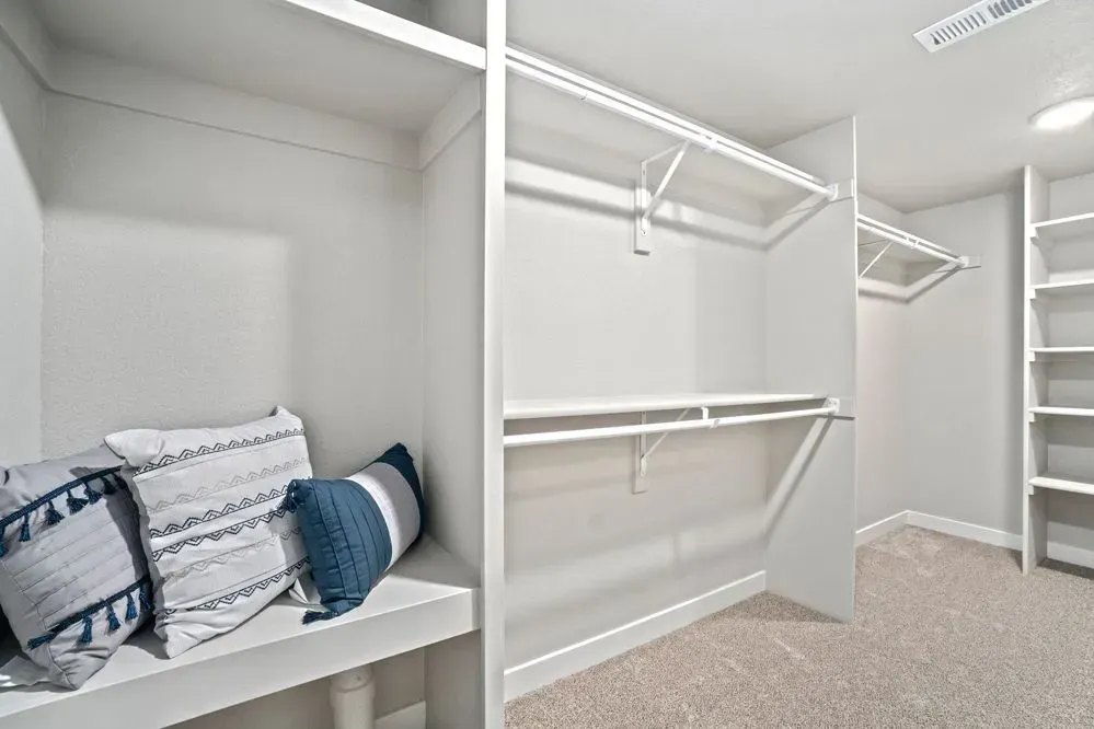 Empty white closet with bench seating and pillows.