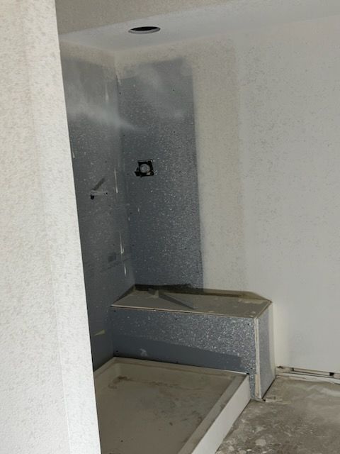 A gray, unfinished shower with a step. The walls are textured, and there's a recessed light.