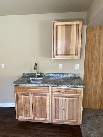 Light wood cabinet with granite countertop, sink, and cabinet on a tan wall with a matching wood cabinet above.