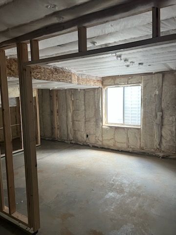 Basement interior under construction with exposed framing, insulation, concrete floor, and a window.