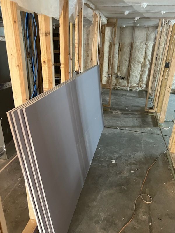 Drywall sheets stacked inside a wood-framed room under construction.