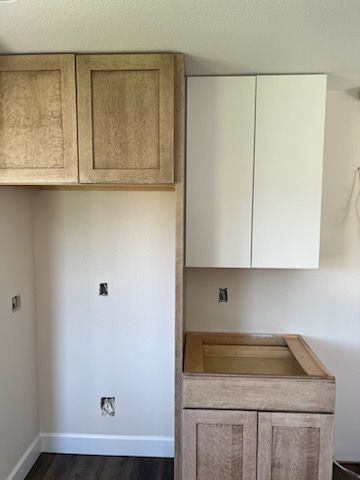Kitchen cabinetry with unfinished wood and white painted cabinets, in a light-filled room.