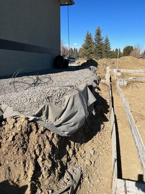Construction site: Gravel over fabric next to building. Wooden forms line the ground.